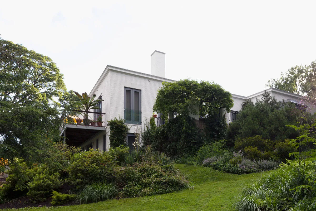 Exterior rear view of the Riverdale Residence showing a white brick facade and extensive garden greenery.