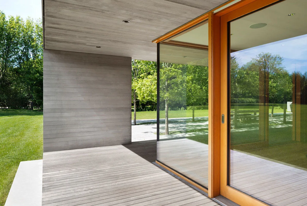 Covered patio with wood decking and concrete ceiling opening to a green lawn through large sliding glass doors.