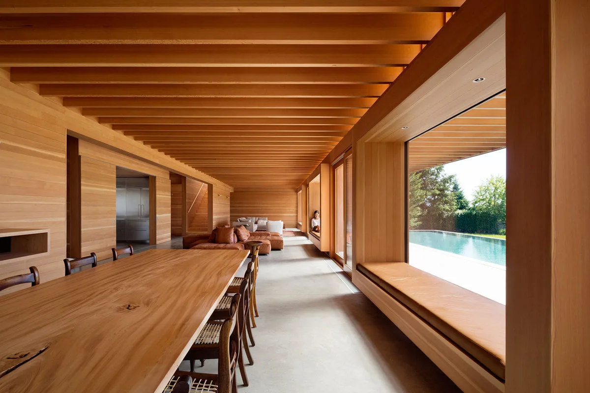 Wood-paneled living and dining area with a low profile sofa, window seating, and a view of the pool.