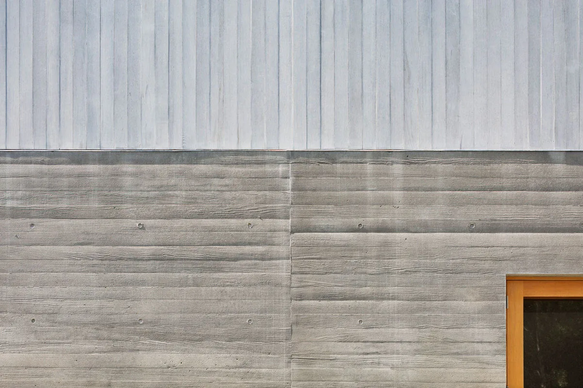 Exterior detail of Watermill Residence shows horizontal board-formed concrete wall and vertical wood siding at upper portion.