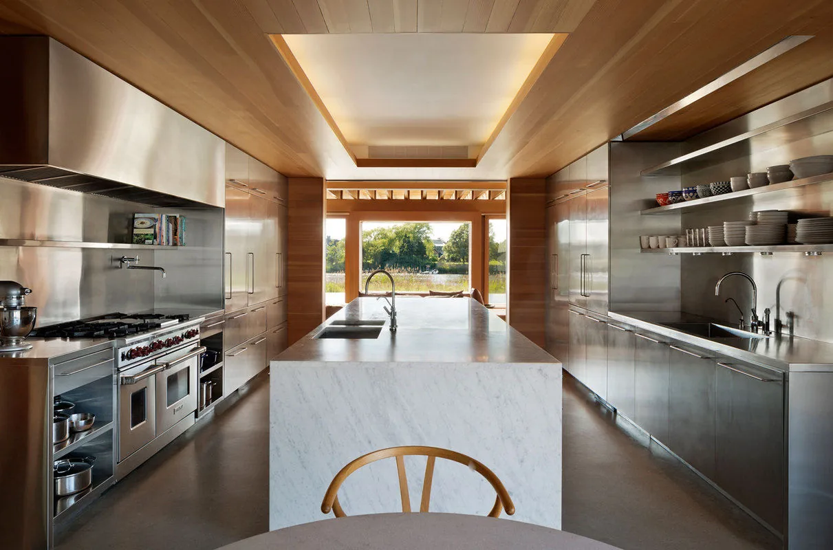 Kitchen in Watermill Residence features stainless steel cabinetry, marble island, and wood ceiling detailing with backlit recessed light.
