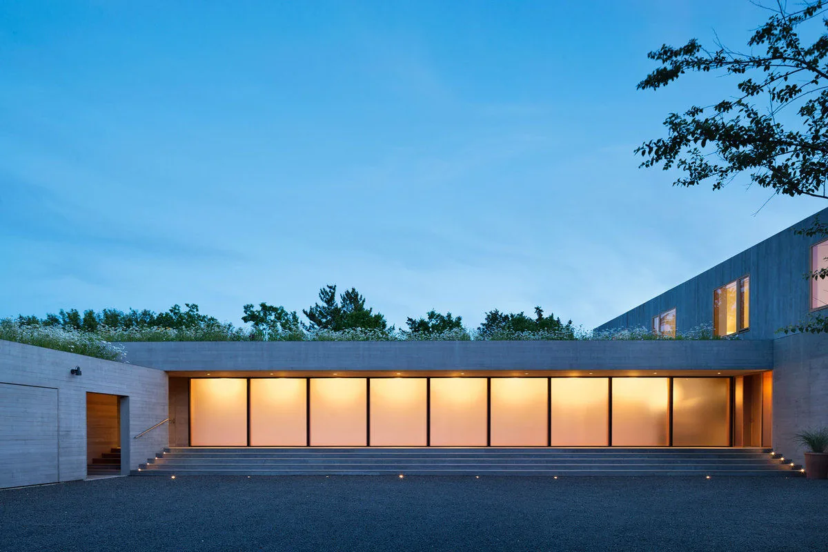 Watermill Residence features a linear layout with square windows softly illuminated from inside under a flat roof.