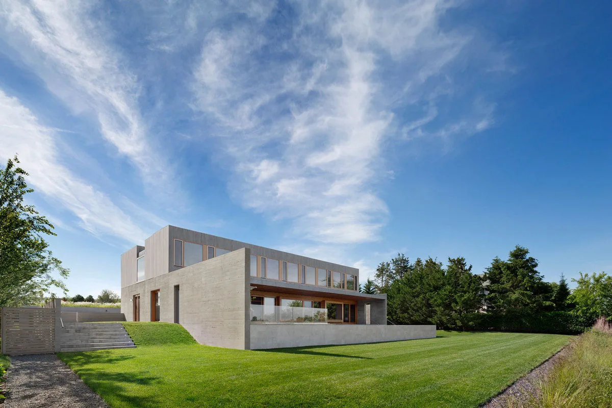 The Watermill Residence features minimalist facade with concrete and wood vertical siding under a flat roof.