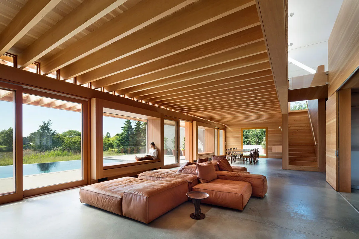 Living room with leather sectional sofa, exposed wood ceiling beams, and large glass sliding doors facing an outdoor pool and garden.