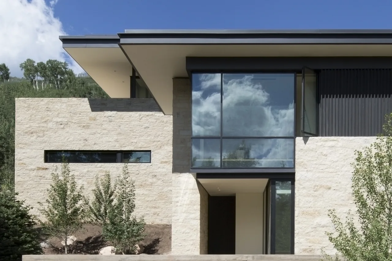Aspen Residence features a modern exterior with floor-to-ceiling glazing and stone walls under a flat roof.