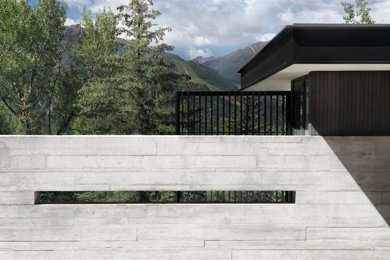 The Aspen Residence features a concrete board-formed wall with a horizontal opening and black window frames under an overhanging flat roof.