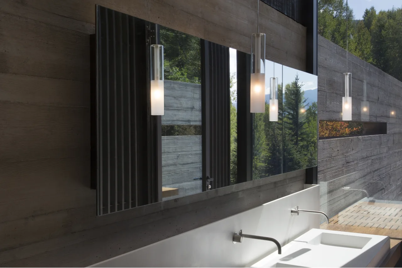 Bathroom in Aspen Residence features wall-mounted faucets, rectangular sinks, pendant lights, and a large mirror with a view to the outdoors.