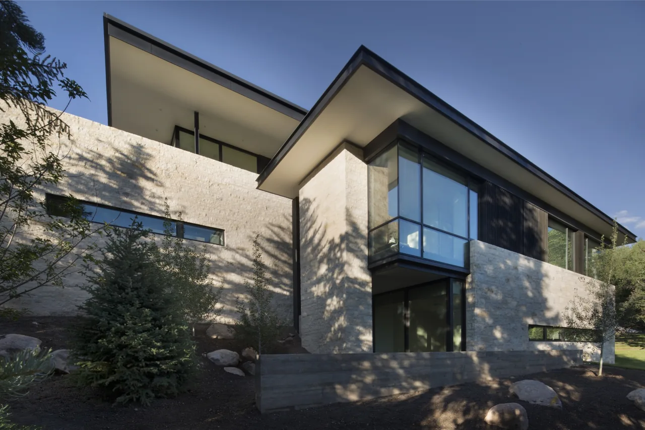 Aspen Residence features stone exterior walls and a cantilevered corner window below an overhanging flat roof.