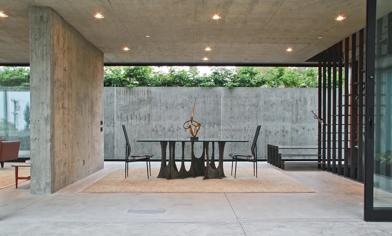 The Cresta dining area features a unique sculptural concrete table base, exposed concrete walls and ceiling, and black metal chairs.