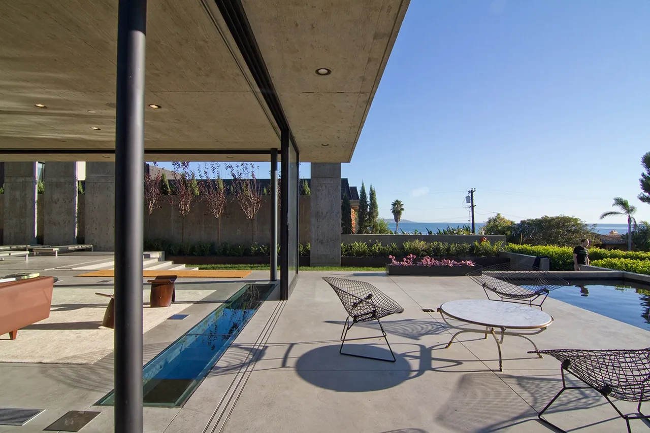 Outdoor living area with concrete flooring, wire chairs, and a pool overlooking the ocean at The Cresta project.