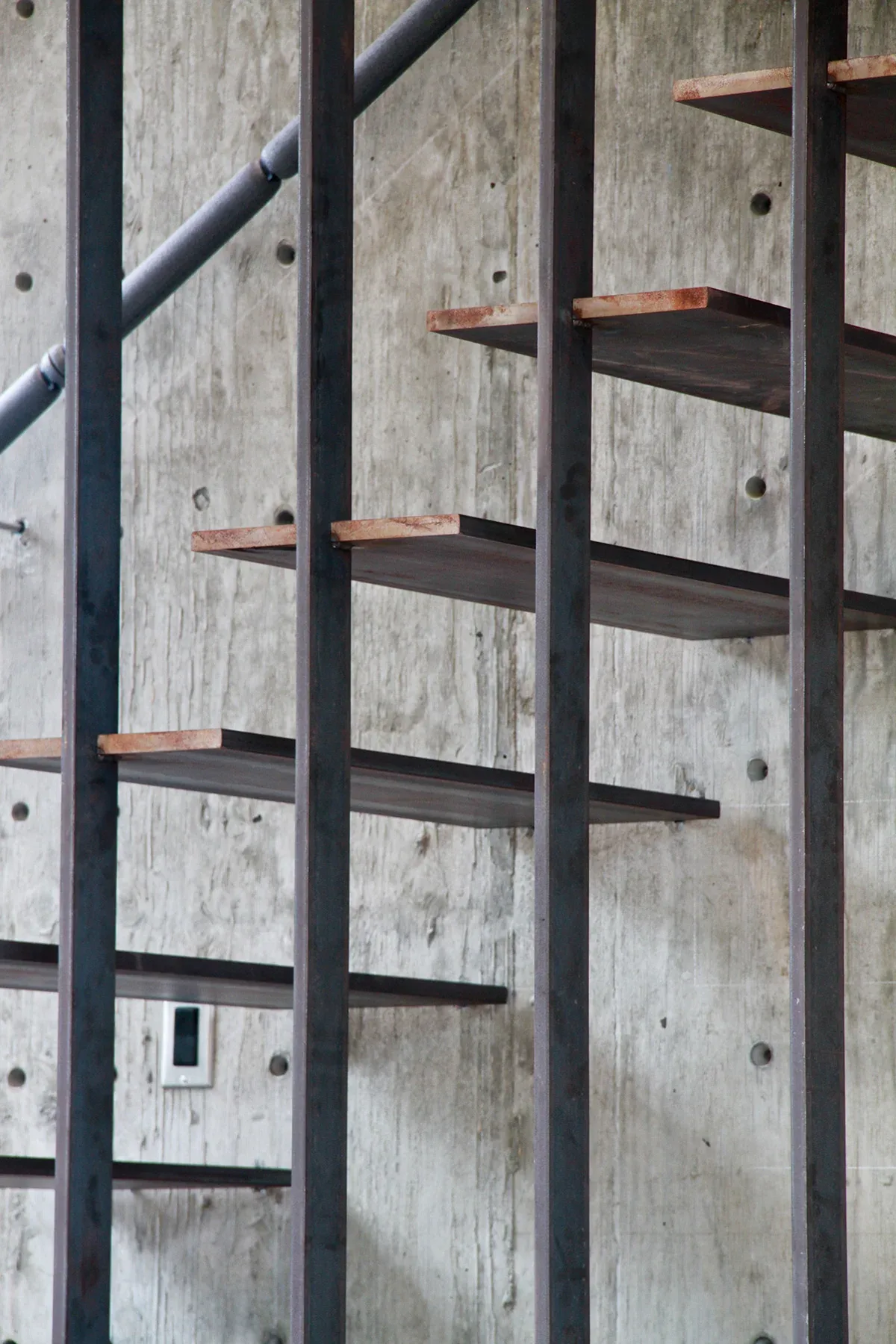 Industrial-style open steel shelving is mounted on an exposed concrete wall with visible anchor points.