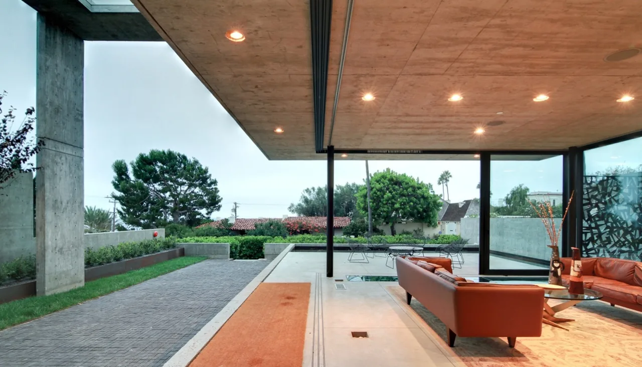 Living room with leather sofas and large glass walls opening to an outdoor patio surrounded by greenery.
