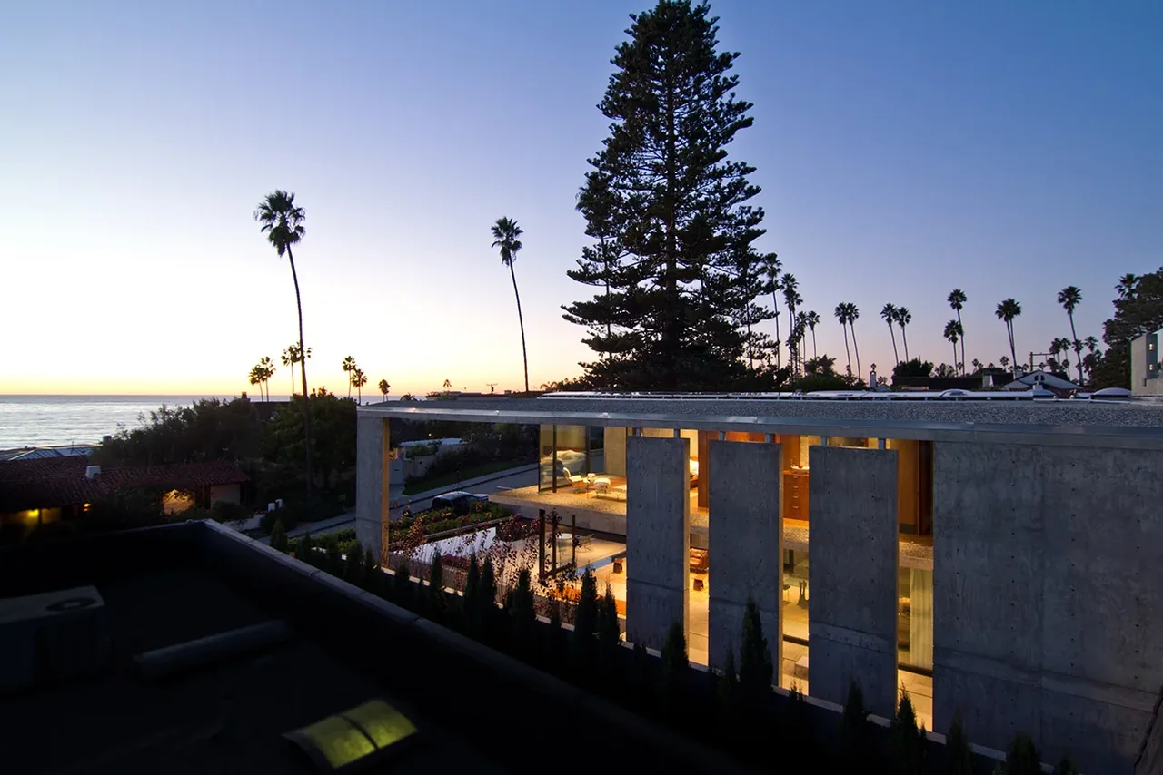 The Cresta features poured concrete walls and floor-to-ceiling vertical windows overlooking the ocean at sunset.