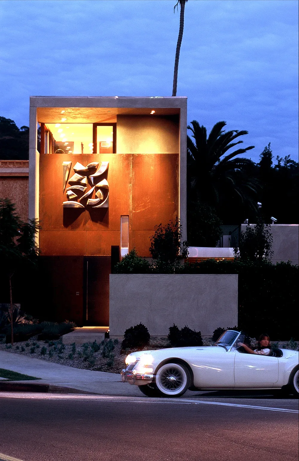 The Prospect, a modern residence with a prominent rust-colored metal facade and illuminated interior, seen at dusk.