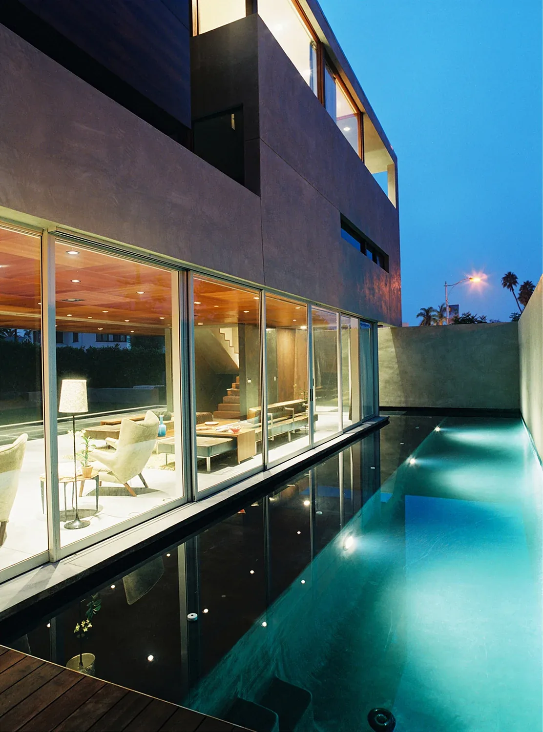 Modern home featuring floor-to-ceiling glazing next to a narrow outdoor pool at dusk.