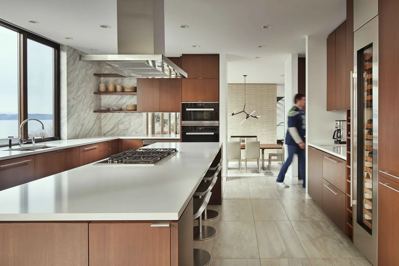 Kitchen features a large white island with gas cooktop, wood cabinets, marble backsplash, and a view of the water.