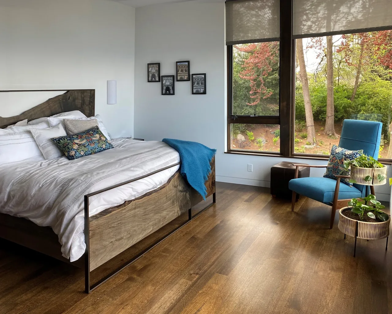 Woodway project bedroom with natural wood bedframe, blue armchair, and large windows showing outdoor greenery.
