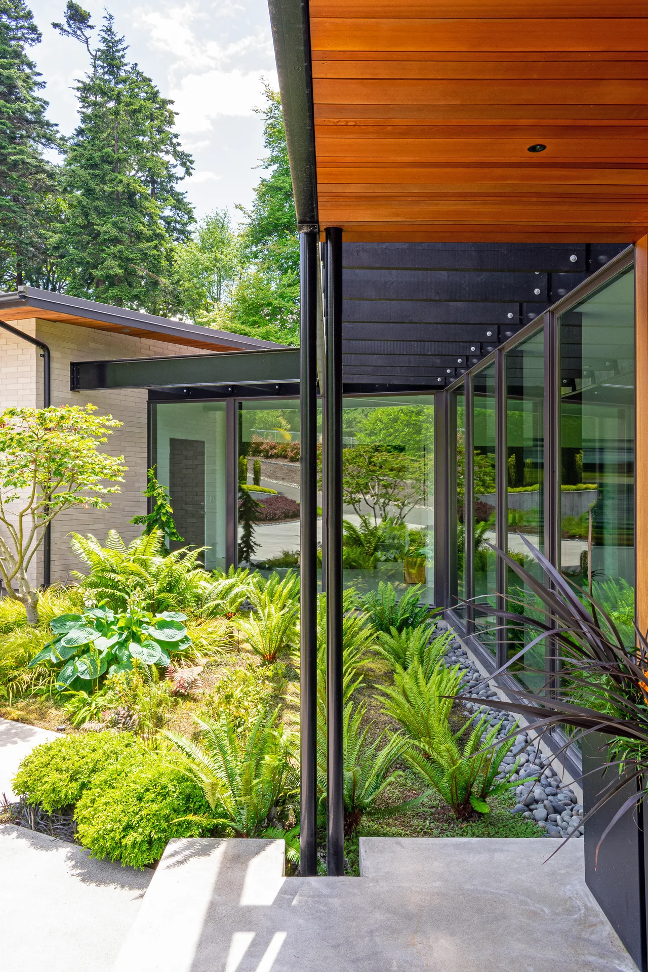 Modern courtyard with floor-to-ceiling glass walls, wood ceiling, and landscaped greenery.