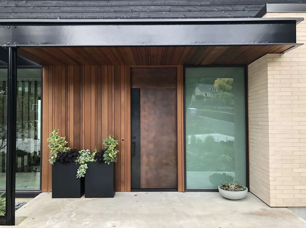 Modern entryway features vertical wood siding, a rust-colored metal door, and large frosted glass window.