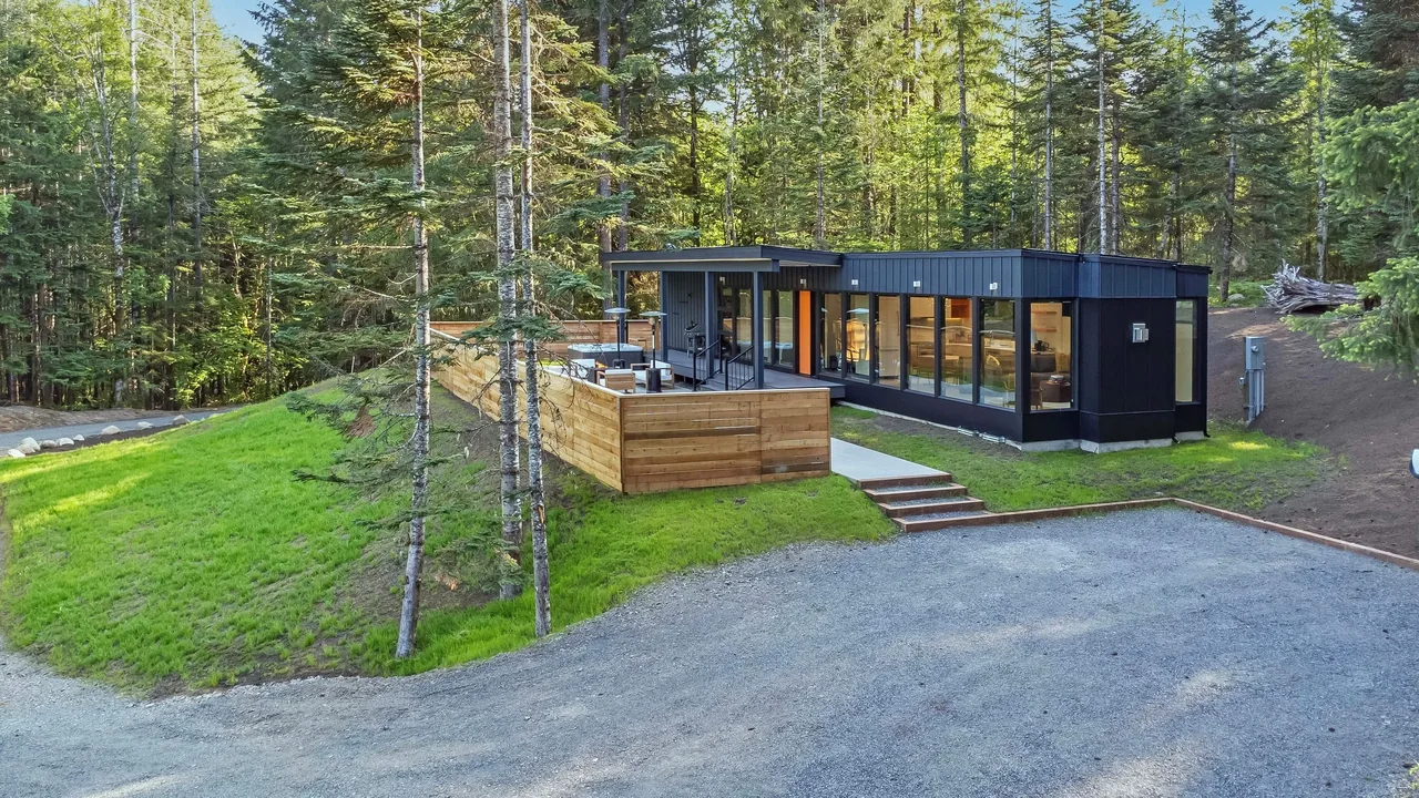 The Getaway Cabin features black steel siding, large windows, and a spacious wood deck amid a forested landscape.