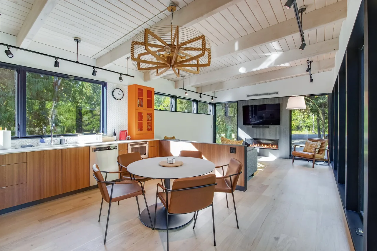 Daylit kitchen and living area in the Getaway Cabin with wood cabinets, a round dining table, and a modern fireplace under a mounted TV.
