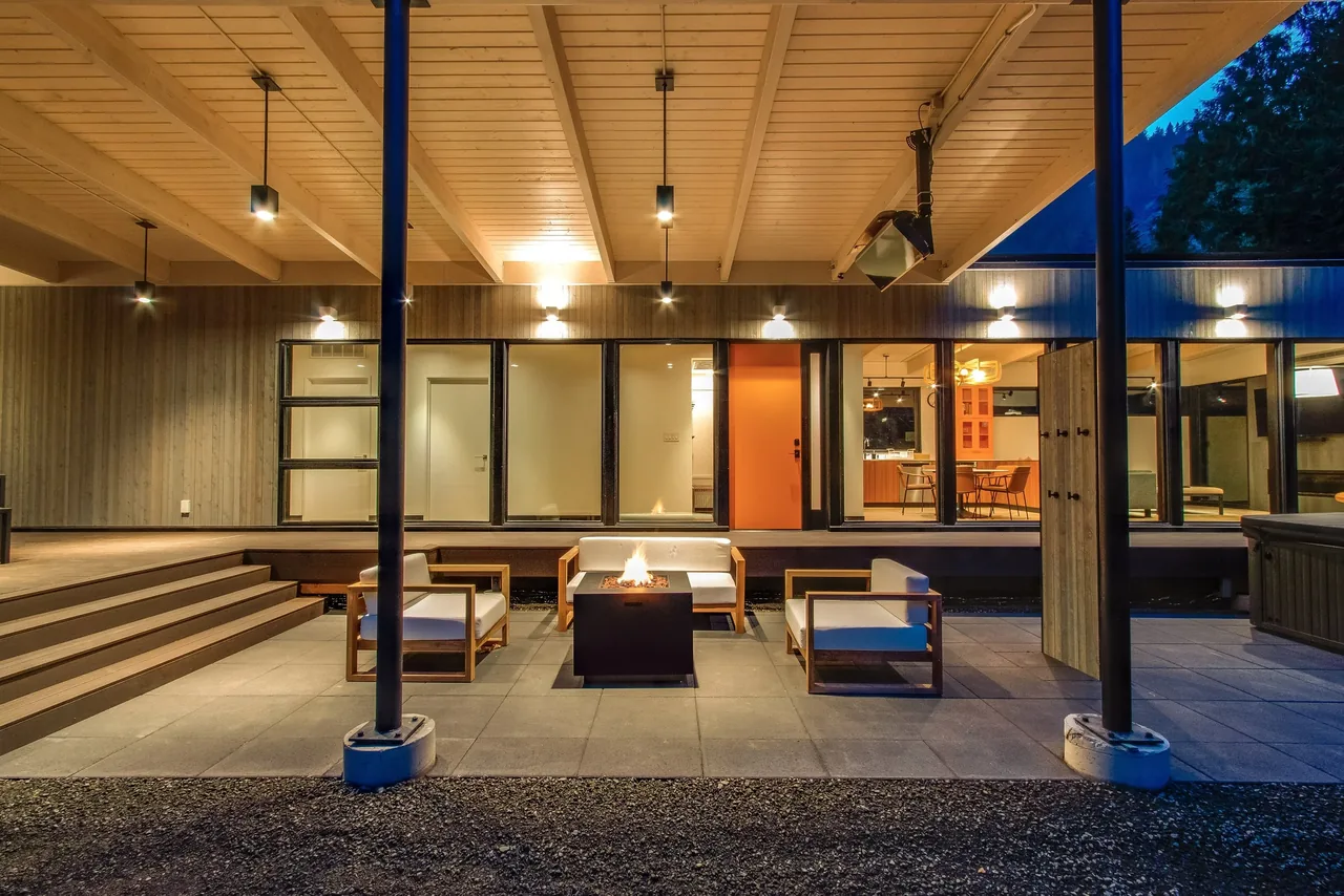 Covered patio area with modern seating and fire pit, adjacent to large glass doors leading to the interior dining area.