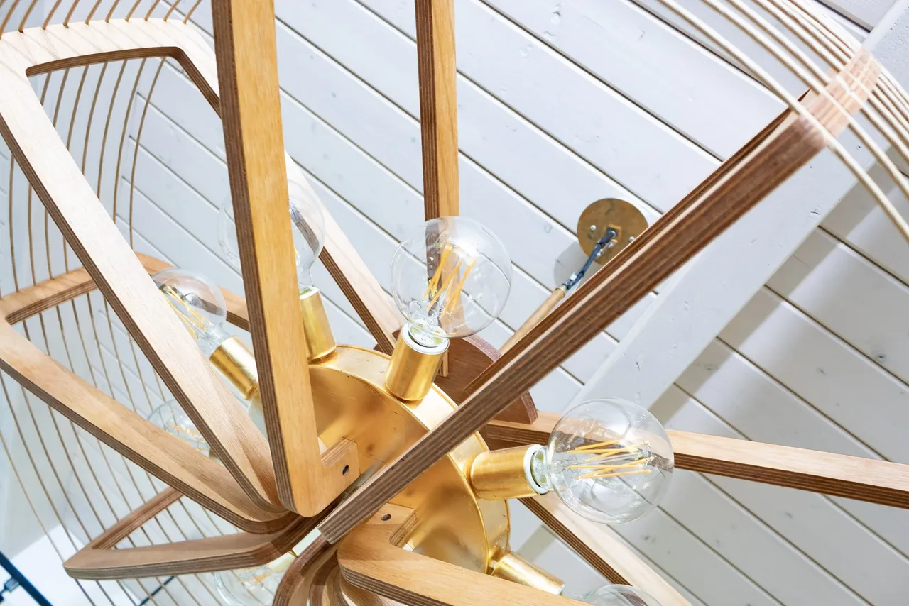Modern chandelier with wooden frame and exposed bulbs hangs from white paneled ceiling.