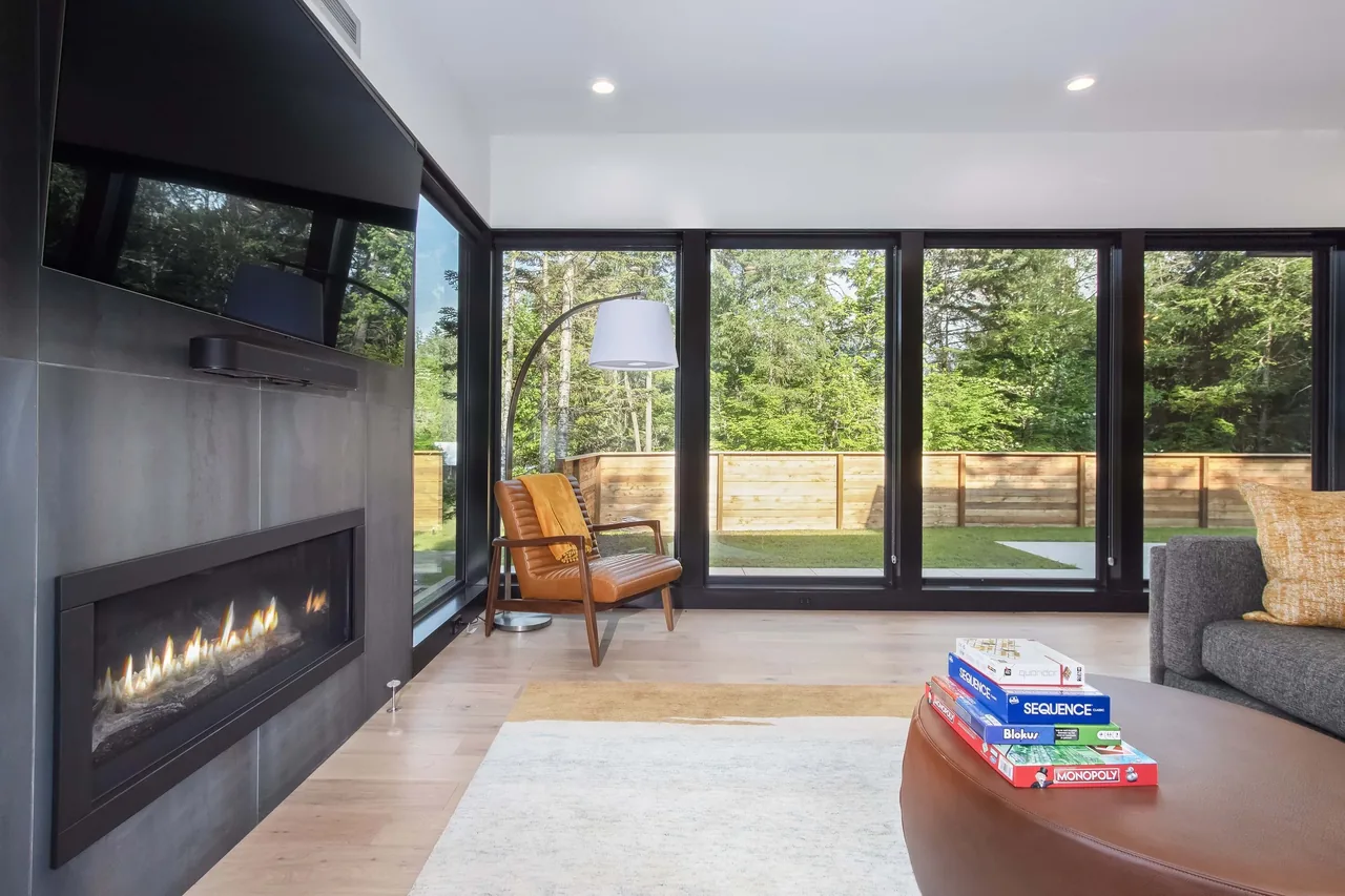 Living room features a linear fireplace, floor-to-ceiling black-framed windows, and a leather chair with an arc floor lamp.