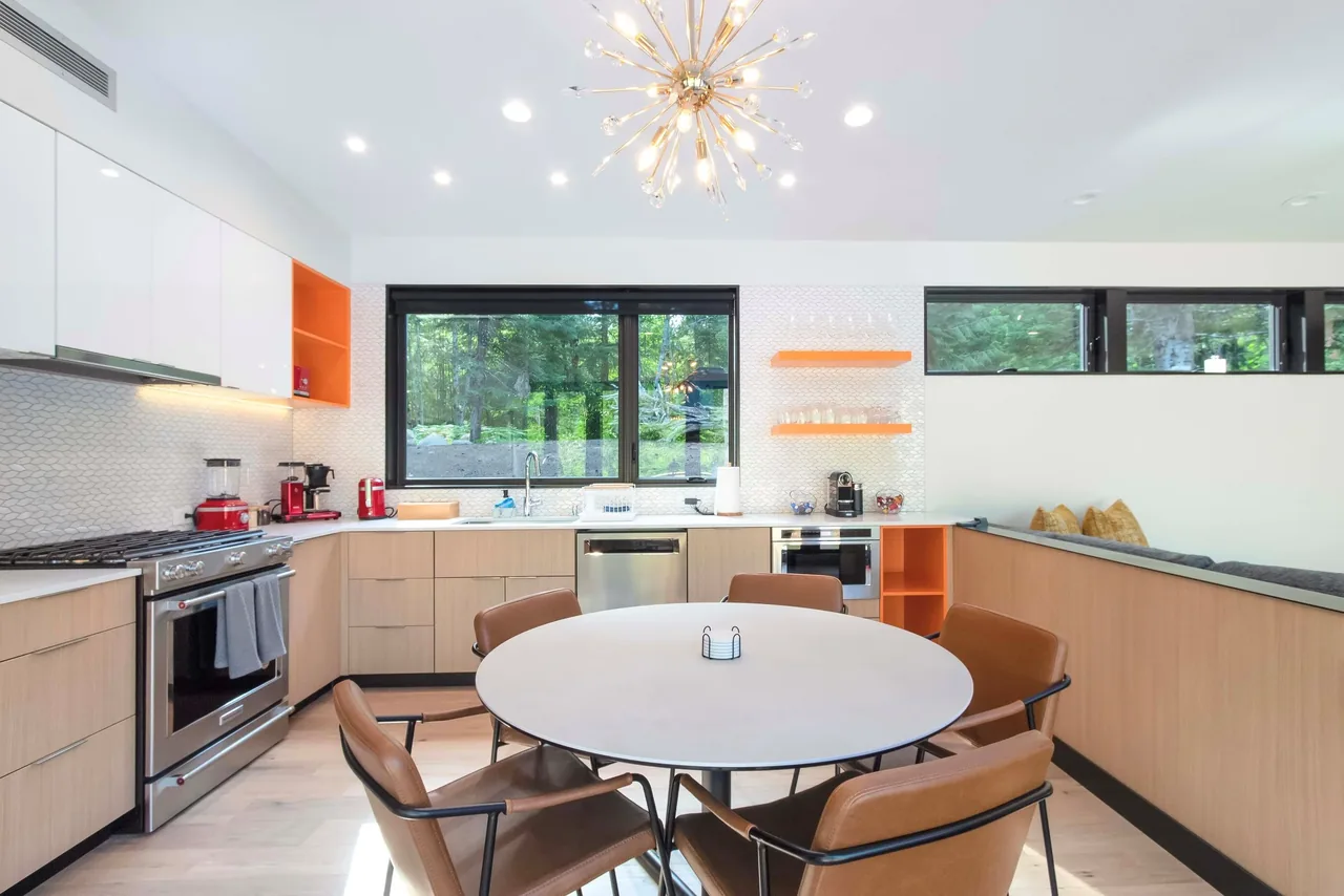 Modern kitchen and dining area with wood cabinetry, white countertops, orange accents, and stainless steel appliances.