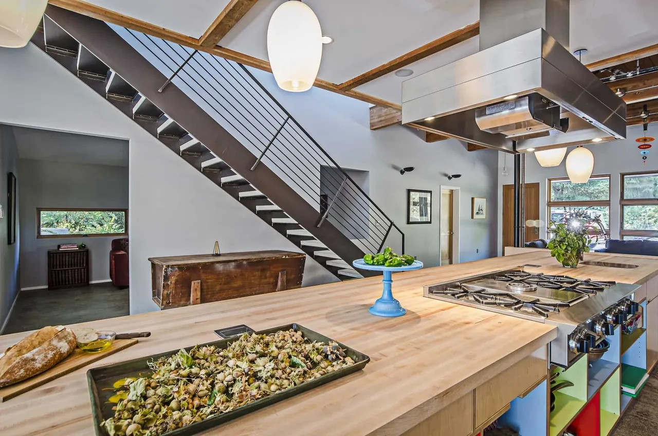 Kitchen with wooden island and metal floating stairs in a modern style home with exposed wood beams.
