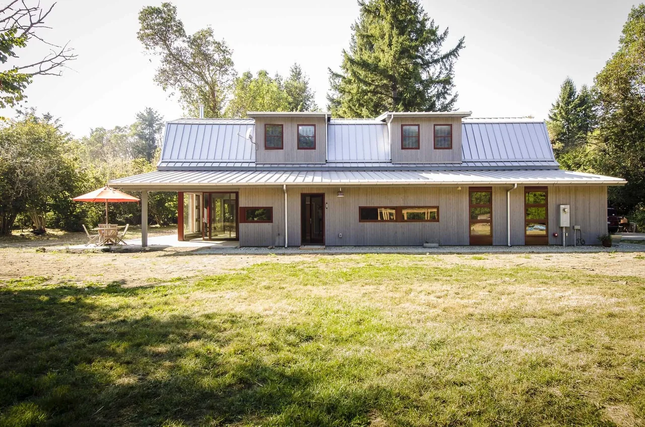The Vashon project by Floisand Studio features a gambrel roof with metal panels and red-framed windows on the exterior.