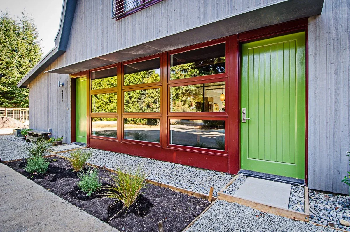 Exterior facade of the Vashon project with red window frames, green door, wood siding, and a gravel garden bed.