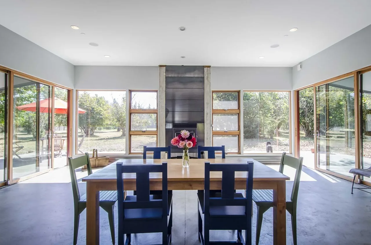 Dining room with wooden table, blue and green chairs, and large windows showing a green outdoor area.