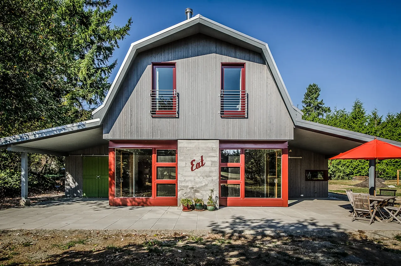Vashon project shows a barn-style house with red window frames, concrete accent wall, and a covered patio area with outdoor dining.