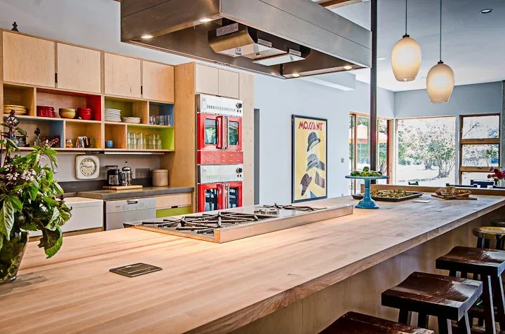 Kitchen featuring a wooden island with a built-in gas range and pendant lights, open shelving, and red double wall ovens.