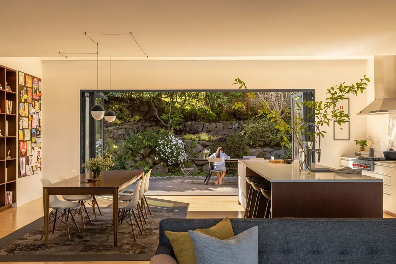 Open kitchen and dining space with a large folding glass wall that opens to a garden patio and stone retaining wall.