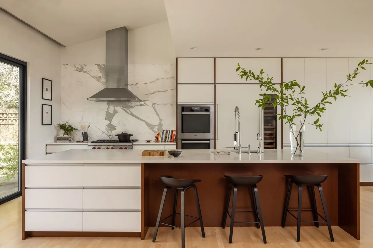 Kitchen featuring a marble backsplash, white cabinets, and a wood-based island with three black bar stools.