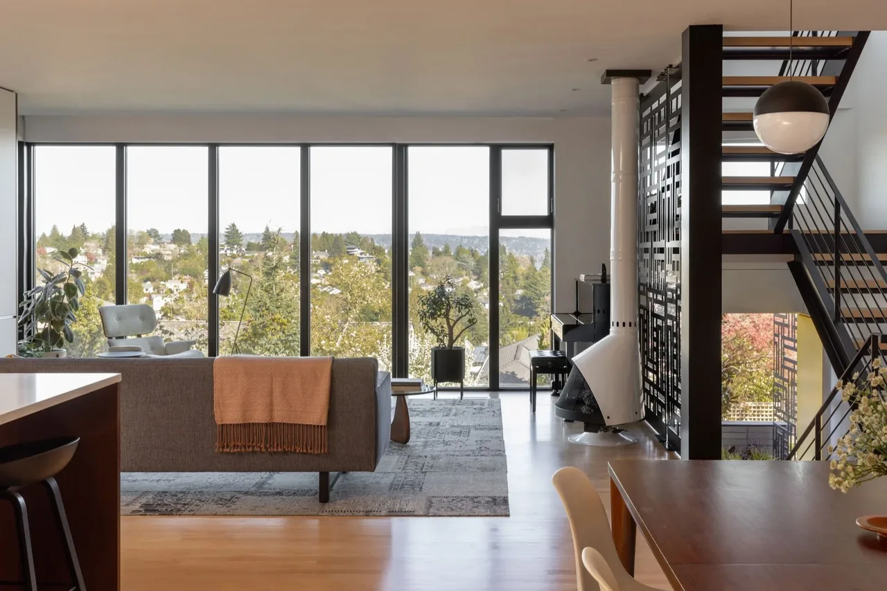 Living and dining area in the 2.0 project by Floisand Studio showcases expansive windows with a view of greenery.