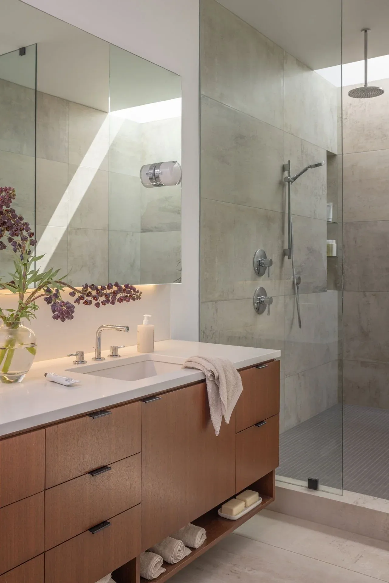 Bathroom features a wood vanity with white countertop and a walk-in shower with large tiles and rainfall showerhead.