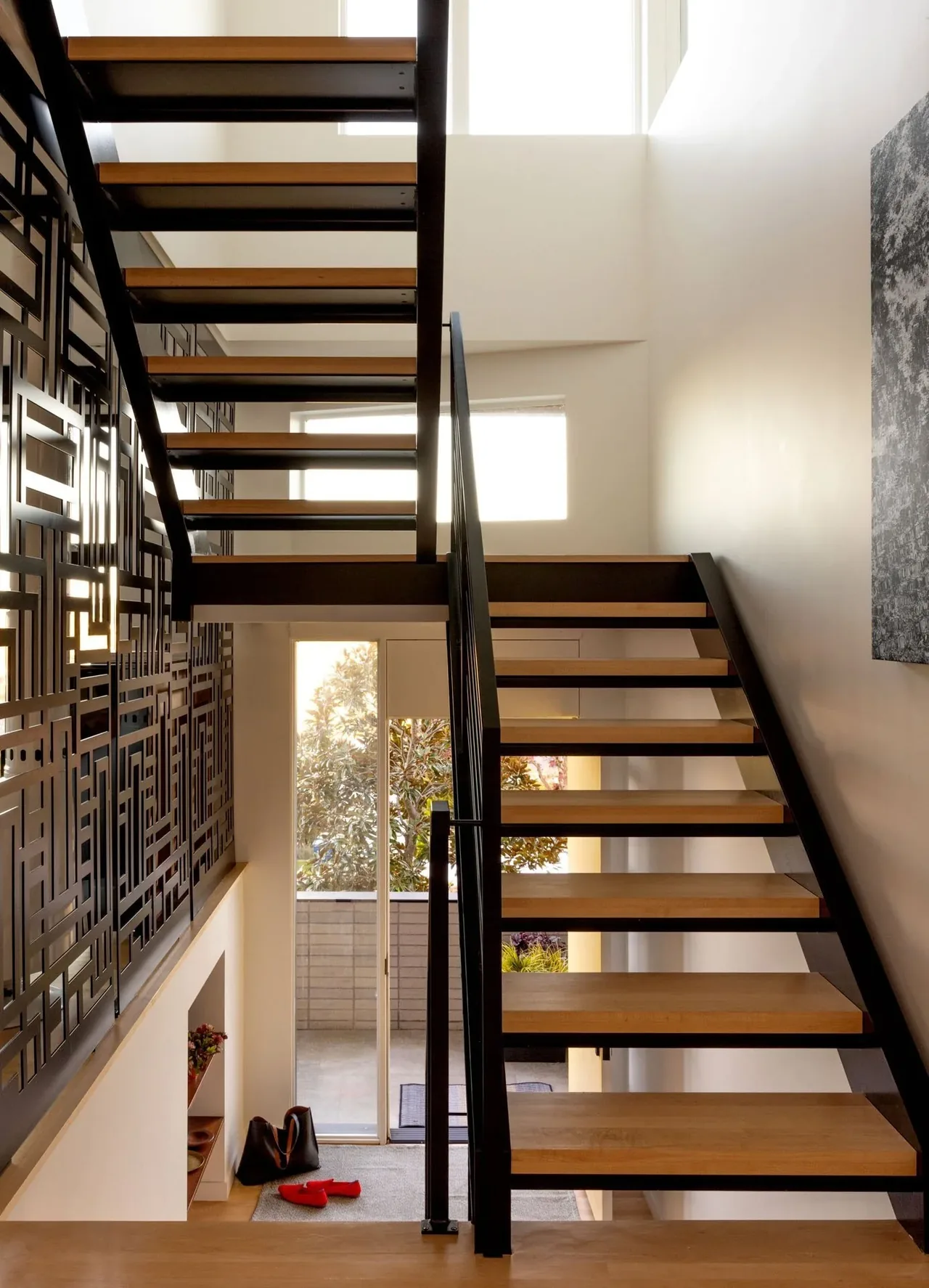 Open riser staircase with black metal and wood treads next to a wall featuring decorative black metal panels.