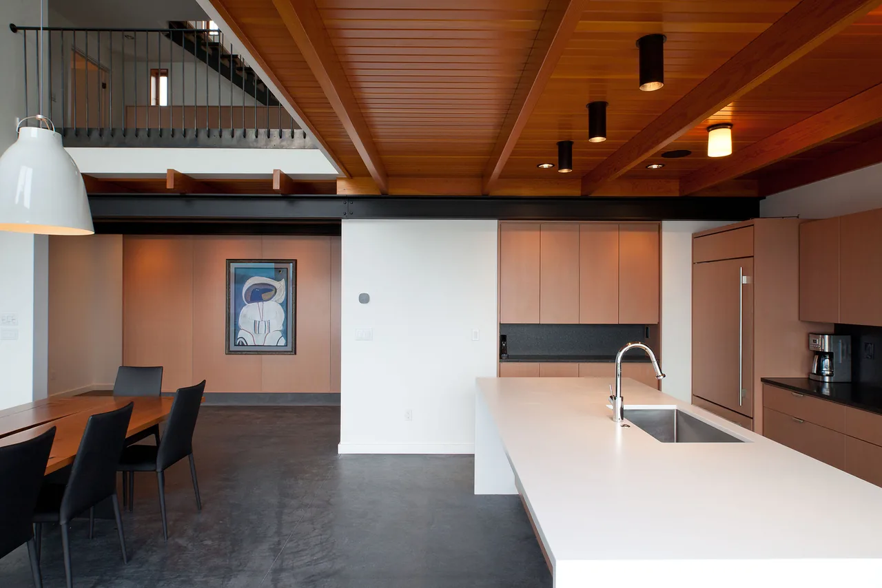 Interior view of the dining and kitchen area featuring a wood-paneled ceiling, minimal cabinetry, and concrete flooring.