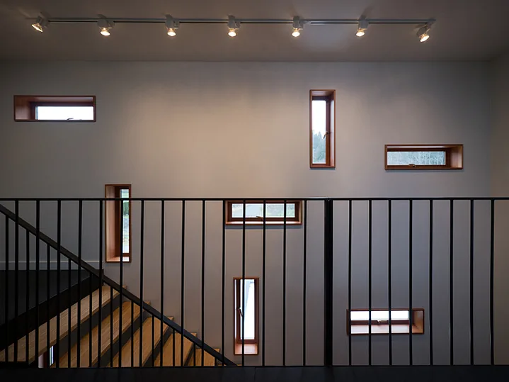 Stairwell features several rectangular wood-framed windows and a black metal railing with track lighting above.