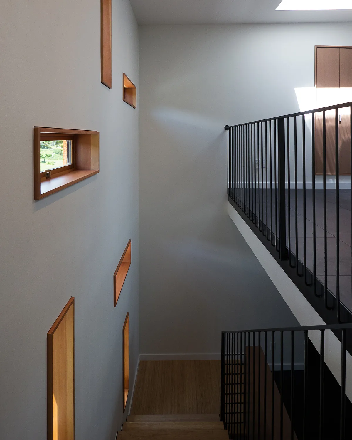Interior stairwell of Whidbey Beach House with small rectangular wood-framed windows and black metal railings.