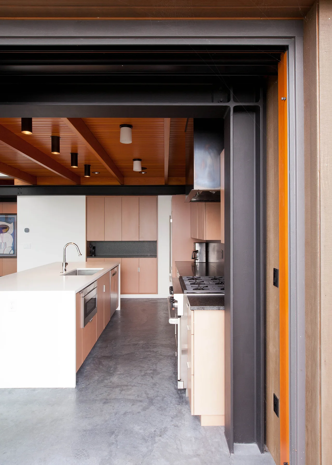 Modern kitchen with wood ceiling panels, a large kitchen island, and polished concrete floors at Whidbey Beach House.