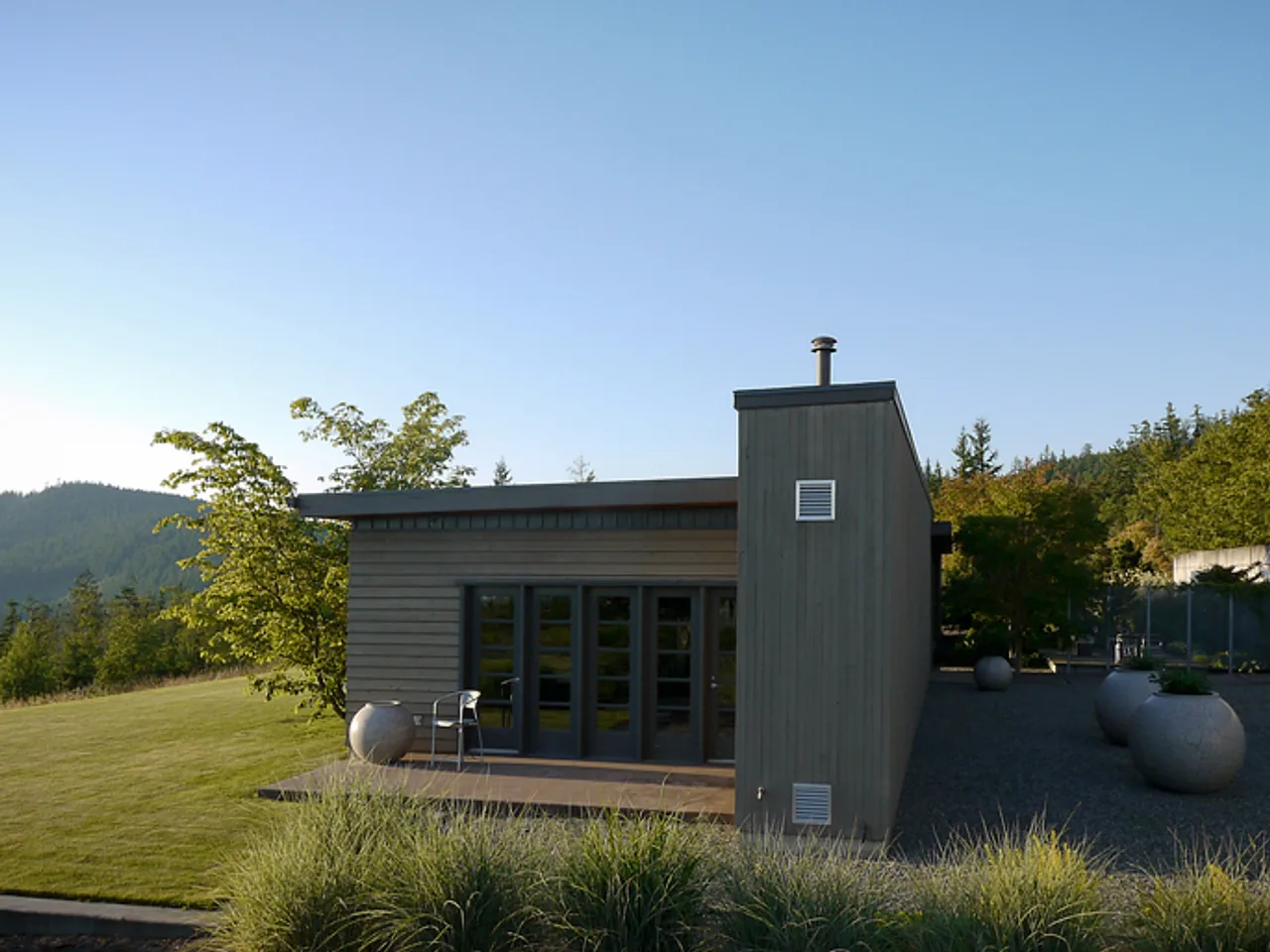 Modern house with wood siding and flat roof seen from the exterior rear, surrounded by landscaping and large planters.
