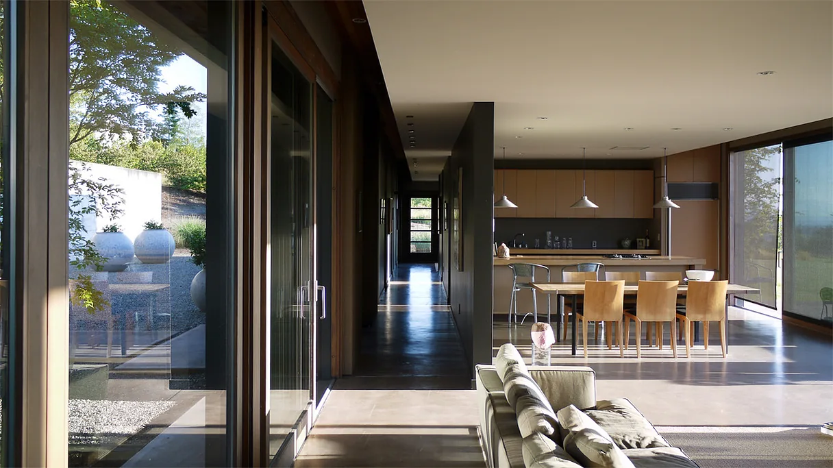 Open living and dining area featuring floor-to-ceiling glazing with views of a landscaped garden and large round planters.