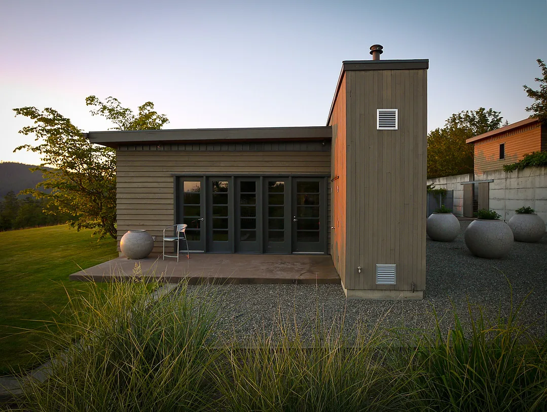 The House, Wall + Garden features wood siding, multiple glass panel doors, and large round planters on the gravel landscape in Seattle.