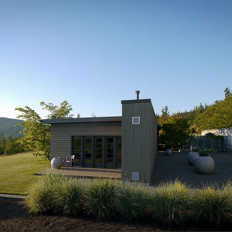 The House, Wall + Garden project features vertical wood siding and glass panel doors opening to a landscaped gravel garden with large round planters.
