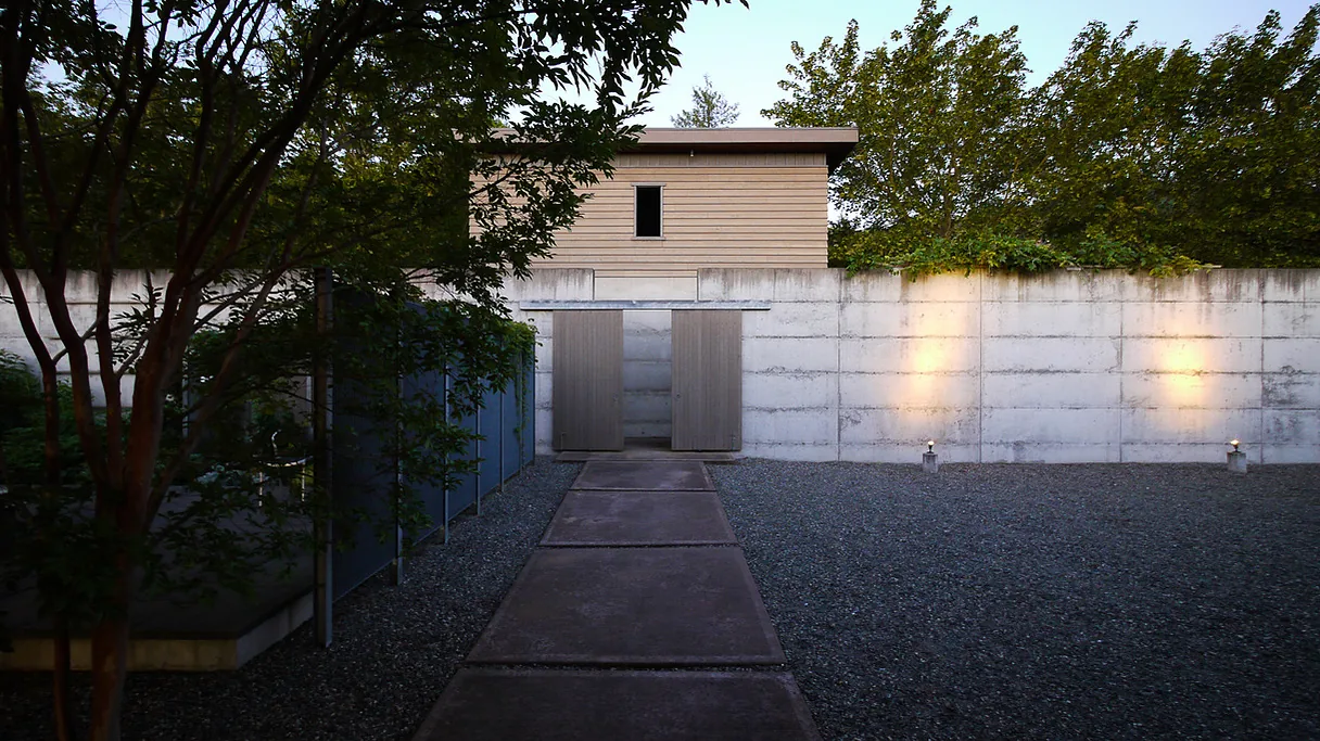 A modern garden courtyard with vertical wood siding above a concrete wall and gravel landscaping.
