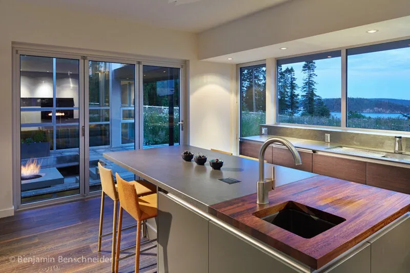 Island Sanctuary kitchen features a spacious island with integrated sink and large windows overlooking a waterfront landscape.